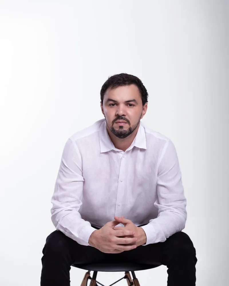 Dr. Firminio Humberto sentado, de camisa branca, com as mãos entrelaçadas