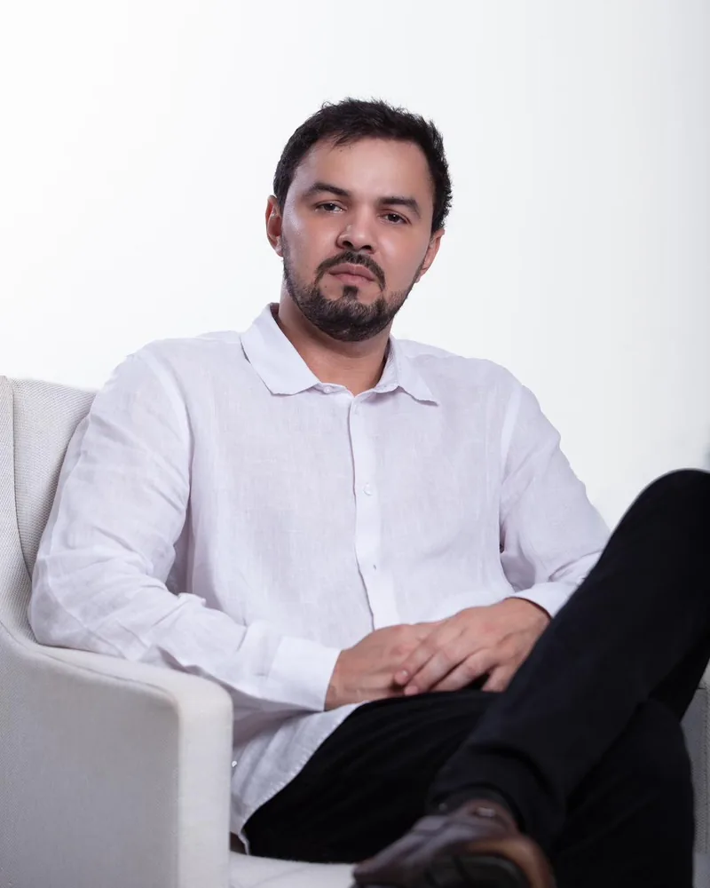 Dr. Firminio Humberto sentado em uma poltrona, de camisa branca